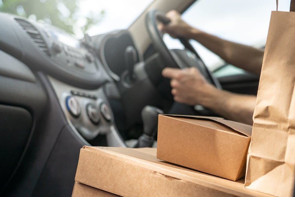 A delivery driver reaching for a packaged online order on the passenger seat