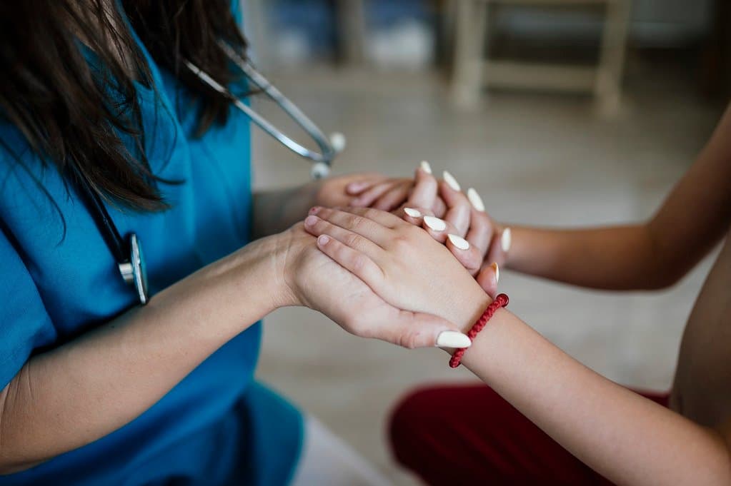 A nurse in scrubs holding a patient's hand during a calm, supportive consultation